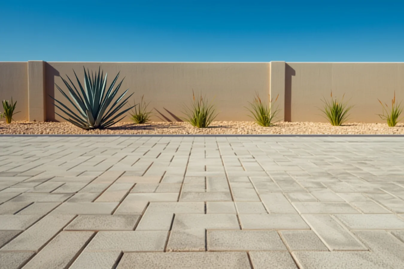 Pale gray and sand concrete pavers in a modular layout of mixed rectangular sizes, edged against a gravel bed of agave and ornamental grass